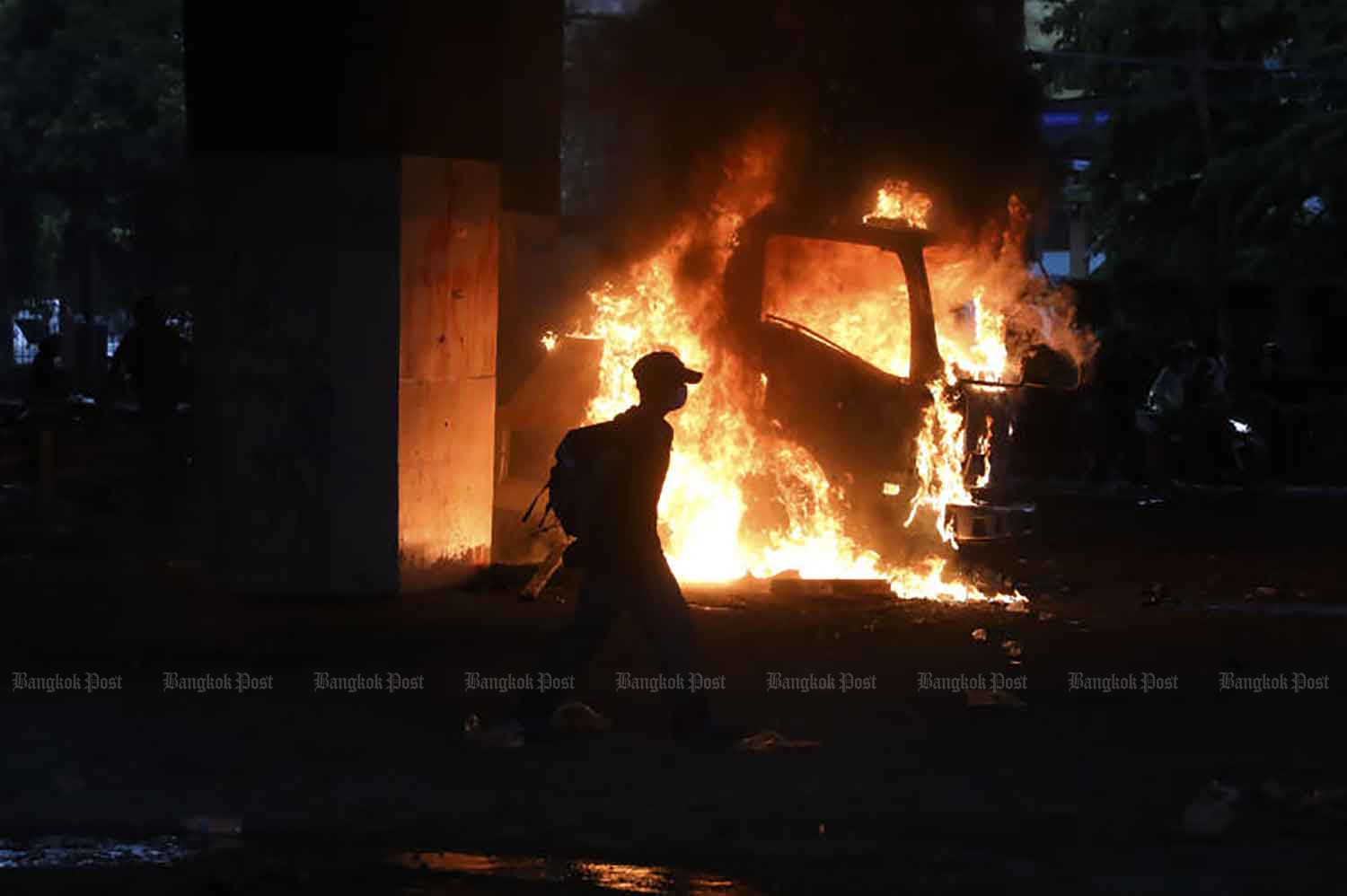 A protester walks past a burning police truck near the Victory Monument in Bangkok on Wednesday evening. (Photo: Arnun Chonmahatrakool)