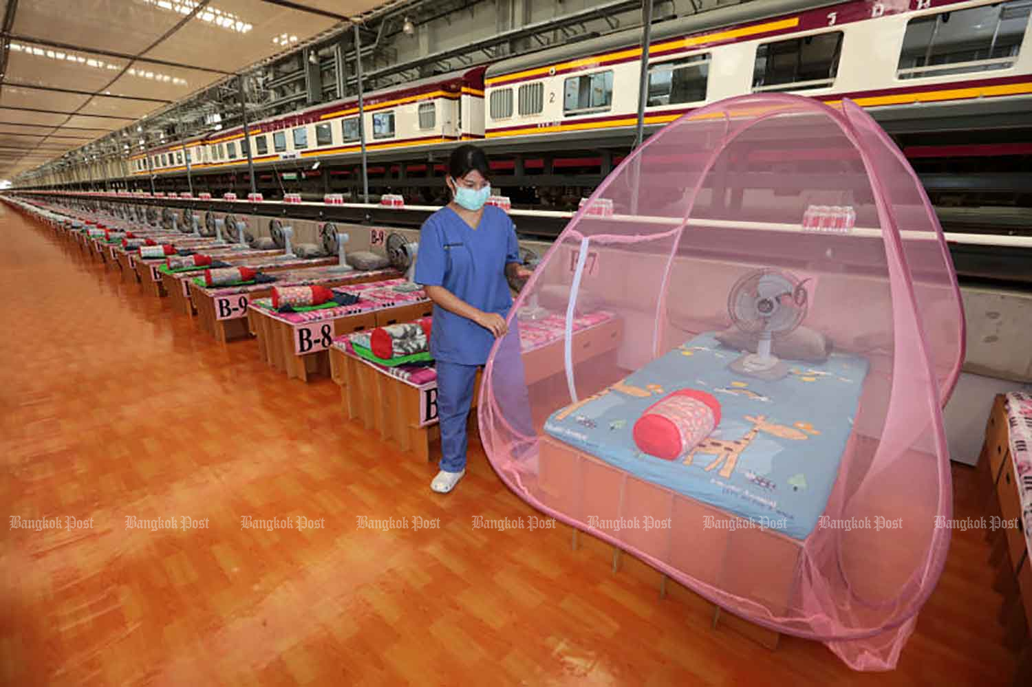 A worker shows how a mosquito net is put up over a bed inside a new community isolation centre at the train maintenance depot at Bang Sue Grand Station in Bangkok on Tuesday. The centre cares for Covid-19 sufferers with few or no symptoms. (Photo: Chanat Katanyu)