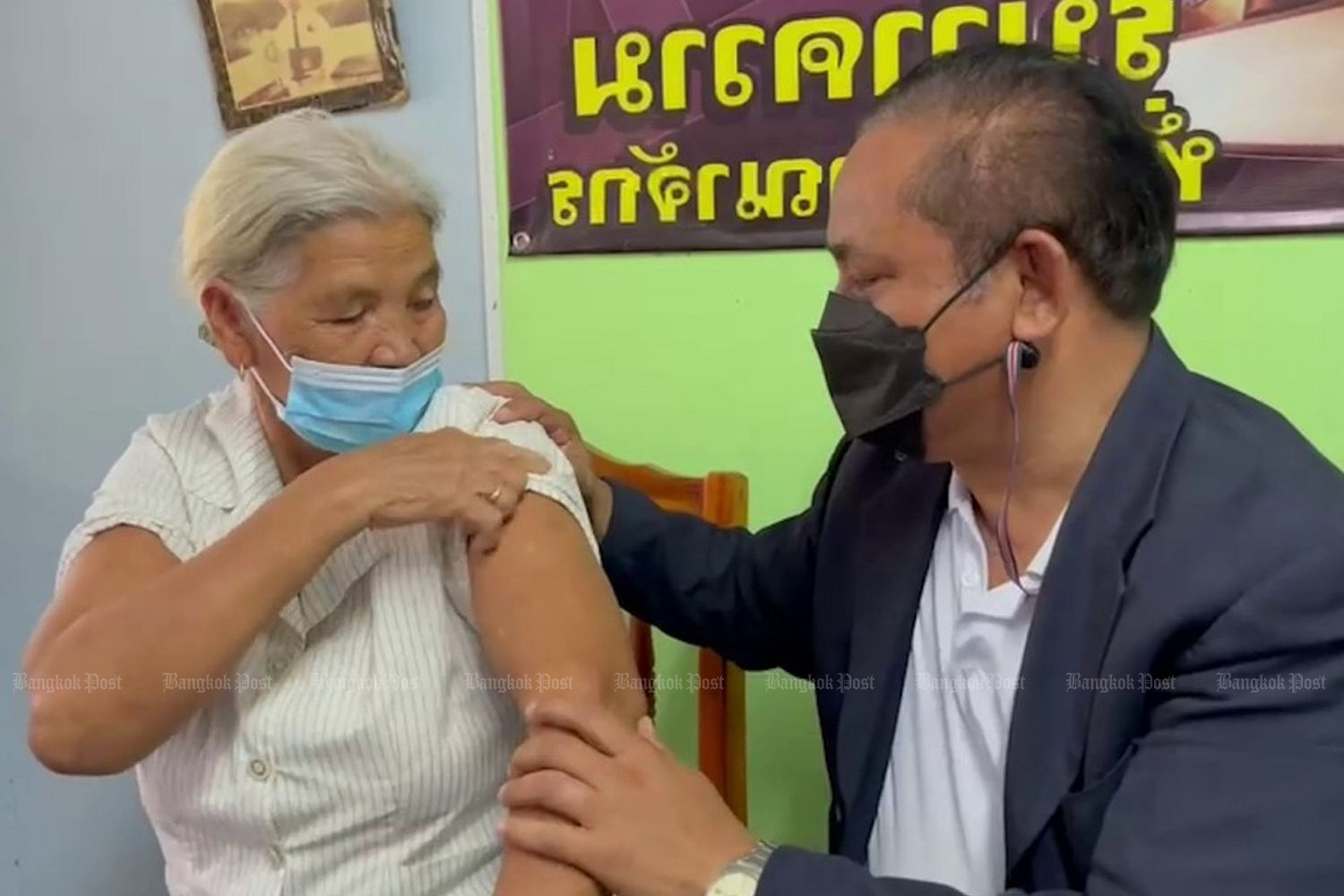 Somwang Jukul (left) shows an arm in a video with her son, while talking to Thai media about how she got two shots of the AstraZeneca vaccine on Saturday.