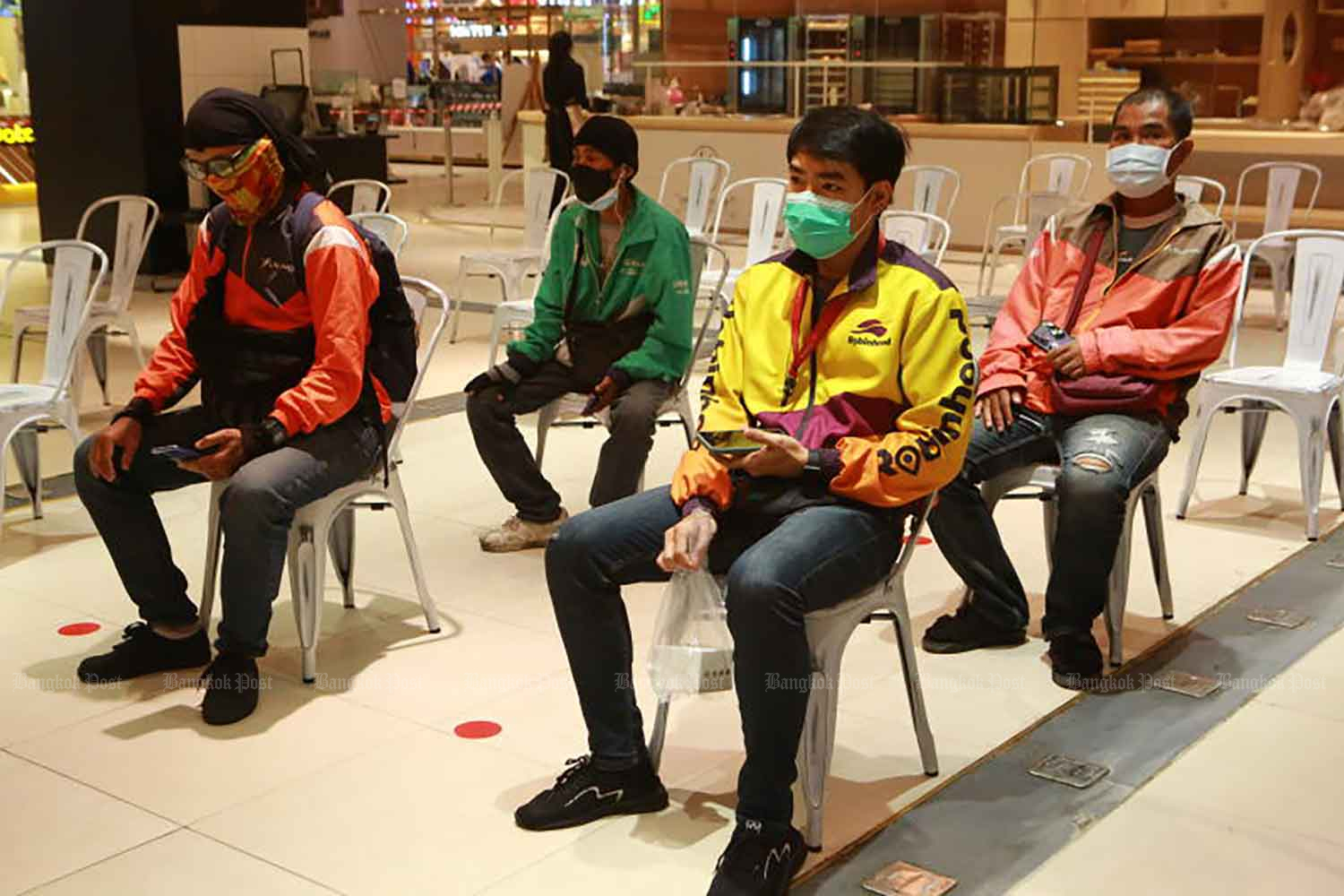 Delivery men wait for food orders at a shopping centre in Bangkok. Dining-in at restaurants in dark-red zones, including Bangkok, has been banned since June 28. (Photo: Somchai Poomlard)