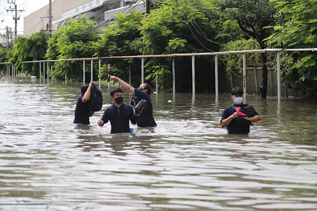 Workers wade through floodwater on Sunday after Saturday night downpours submerged the Bangpoo Industrial Estate in Muang district of Samut Prakan. (Photo: Sutthiwit Chaiyutworakan)