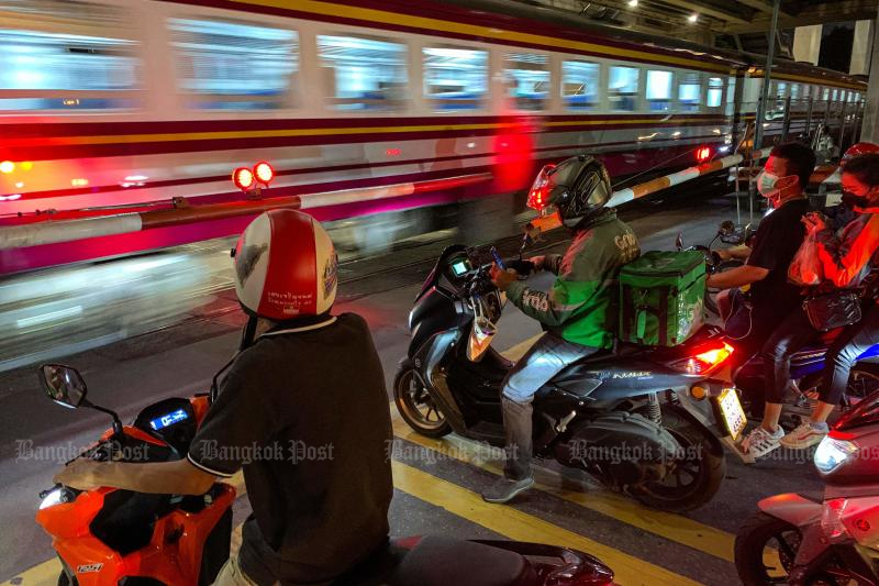 A food rider and other motorists wait for a train to pass through a crossing in Bangkok on Wednesday. Food delivery booms in Thailand after the Covid-19 outbreak forces people to stay at home. (AFP photo)