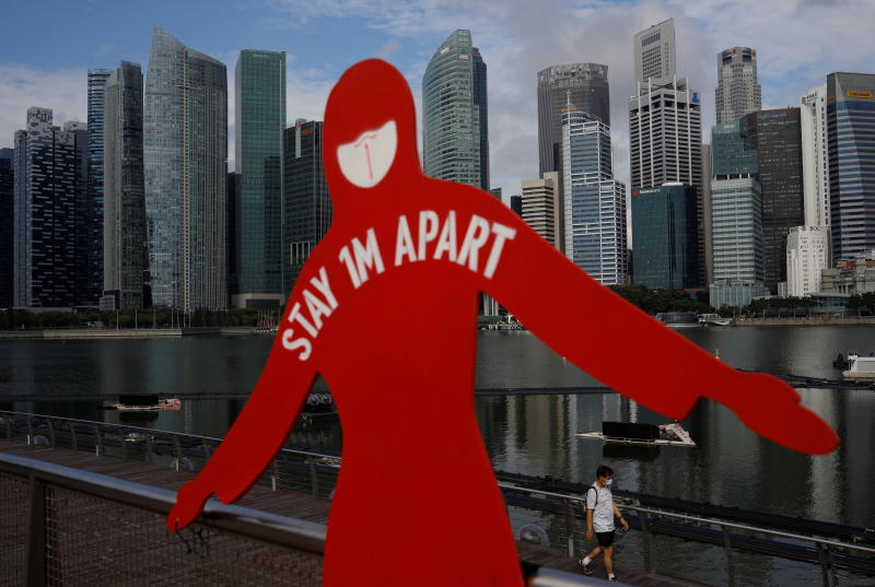 A man wearing a face mask passes a sign put up to encourage social distancing during the coronavirus outbreak, at Marina Bay in Singapore, on Wednesday. (Reuters photo)