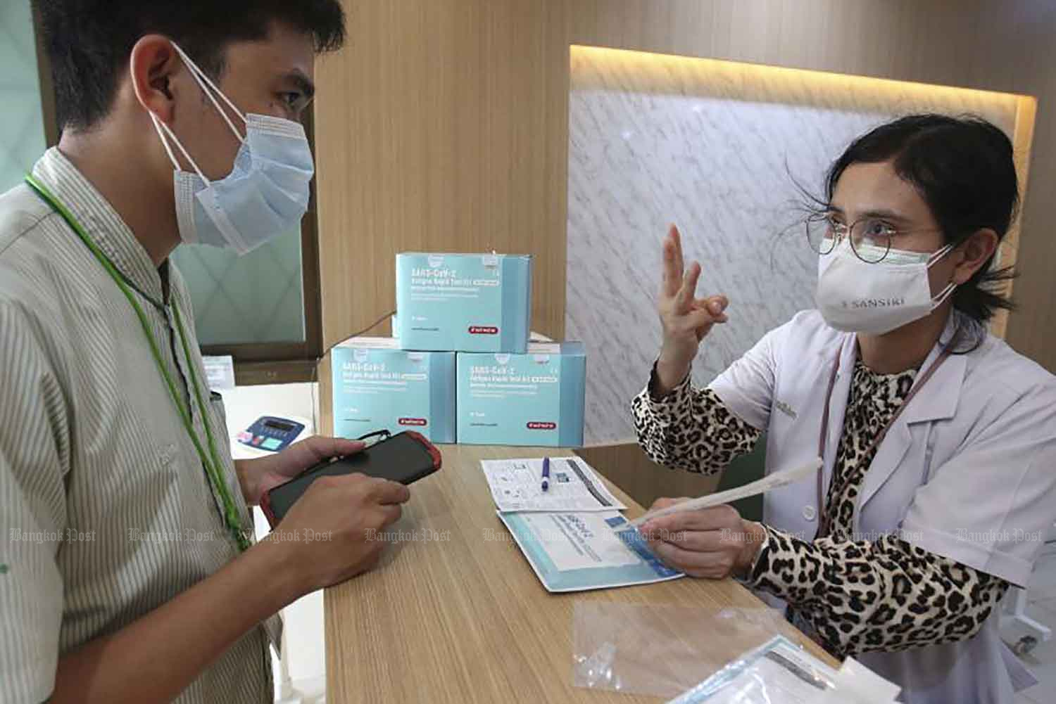 A chemist at a pharmacy in Pathum Thani explains the correct way to use an antigen test kit (ATK) to a customer on Tuesday. Authorities are urging those who have received free ATKs from the government to take the test, instead of reselling them or letting them go to waste. (Photo: Pattarapong Chatpattarasill)