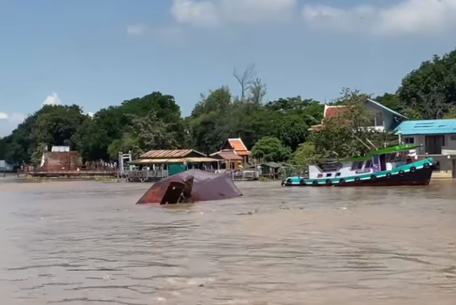 The overturned tugboat in the Chao Phraya River in front of Wat Phanan Choeng Voraviharn in Ayutthaya province on Wednesday morning. The boat driver and his wife were missing. (From video posted on @Ayutthayaruamjai rescue Facebook page)