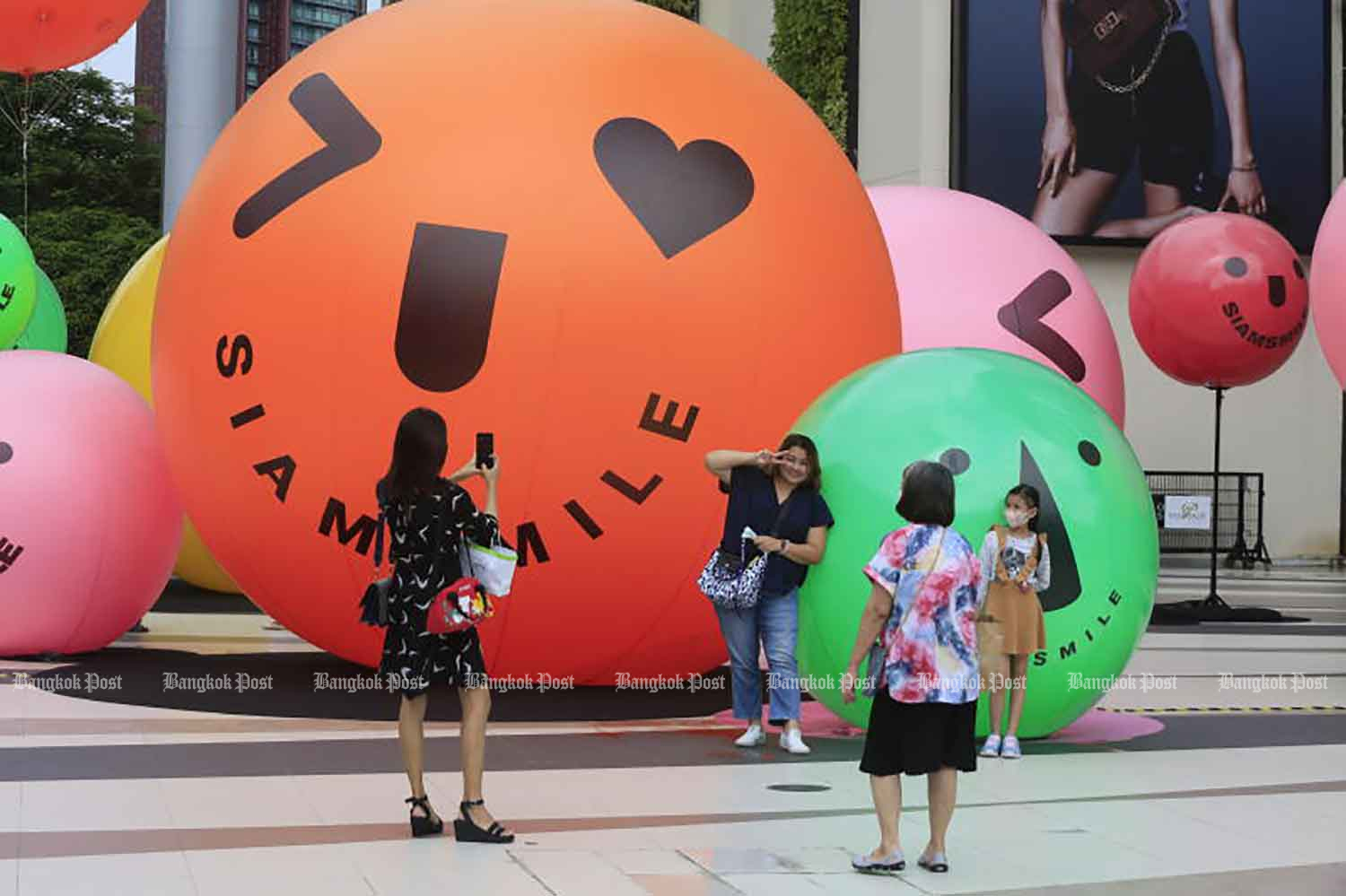 People take photos in front of Siam Paragon shopping centre in Bangkok's Pathumwan district of Bangkok on Tuesday. Officials plan to allow shopping centres and other venues to organise events with at least 50 participants on Saturday. (Photo: Pornprom Satrabhaya)