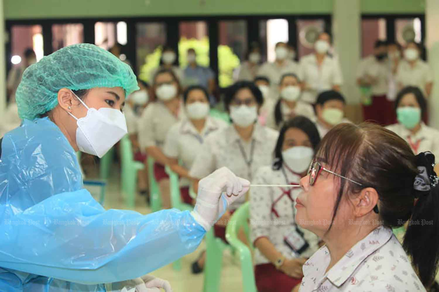 A medic at Kluaynamthai Polyclinic demonstrates how to use an antigen test kit to 200 teachers and educational personnel at Wattana Wittaya Academy on Sukhumvit Soi 67 on Monday. The National Health Security Office (NHSO) is also subsidizing some of the cost of the ATKs for educators. (Photo: Apichart Jinakul)
