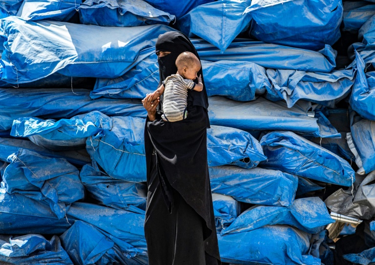 A woman wearing a niqab (full face veil) walks carrying an infant at al-Hol camp for displaced people in al-Hasakeh governorate in northeastern Syria on July 22, 2019, as people collect UN-provided humanitarian aid packages. A woman wearing a niqab (full face veil) walks carrying an infant at al-Hol camp for displaced people in al-Hasakeh governorate in northeastern Syria on July 22, 2019, as people collect UN-provided humanitarian aid packages.