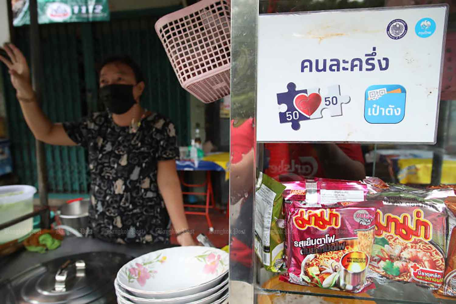 A sign for the government's Khon La Khrueng co-payment subsidy scheme is seen at a noodle stall. The subsidy offers up to 150 baht cash back per person per day for food, drink and general goods purchases. (Photo: Arnun Chonmahatrakool)