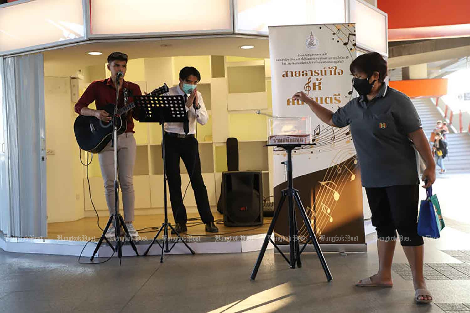 Two musicians busk at Mo Chit station while a commuter drops money in a collection box on Thursday. Bangkok Mass Transit System (BTS) allows musicians to perform at Mo Chit and Phrom Phong BTS stations from the late afternoon to help them earn a living during difficult times for entertainers due to Covid-19 controls. (Photo: Arnun Chonmahatrakool)