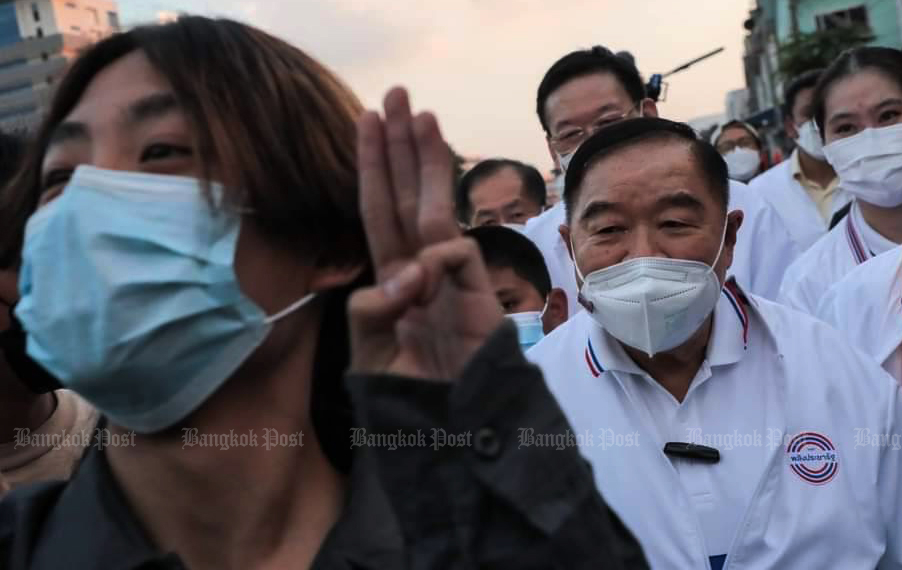 An interloper flashes a three-finger salute, a pro-democracy protest symbol, in front of Palang Pracharath leader Prawit Wongsuwon, who was campaigning in Bang Bua Ruam Jai Pattana community, Bangkok, on Monday. (Photo: Wassana Nanuam)