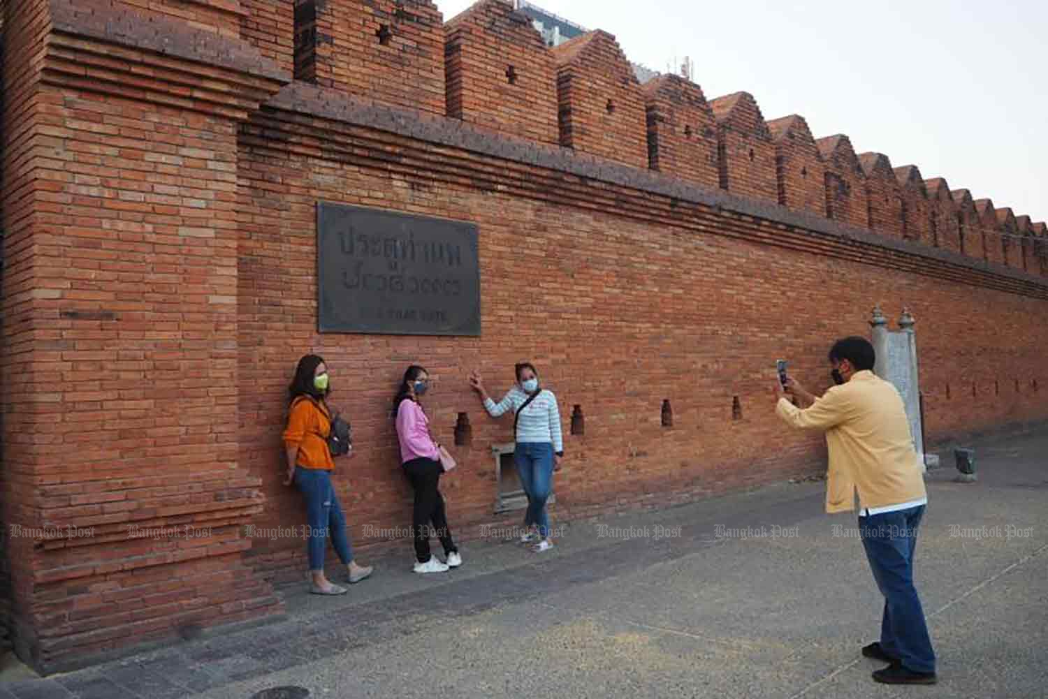 Tourists pose at the Old City Wall in Chiang Mai. The northern province is one of two new pilot tourism areas where disease controls have been eased. (Photo: Dusida Worrachaddejchai)