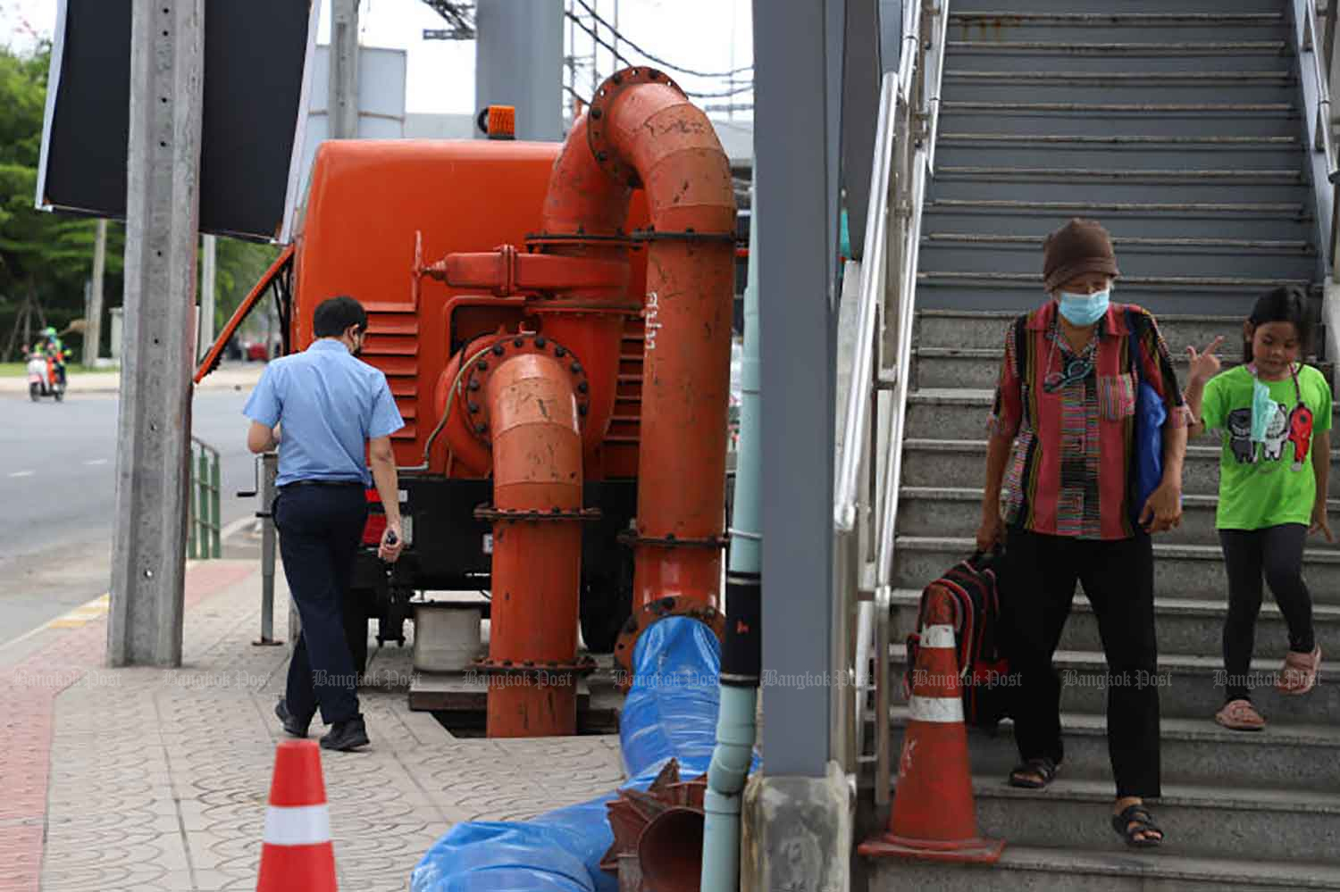 A pedestrian looks at a water pump deployed near Wat Phra Sri Mahathat BTS station on Phahon Yothin Road in Bang Khen district, Bangkok, on Thursday to quickly drain floodwater from the area around Laksi monument. (Photo: Varuth Hirunyatheb)