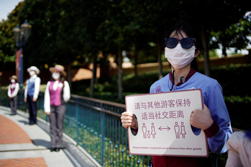 A staff member holds a sign reminding visitors to maintain social distance at the Shanghai Disney Resort in Shanghai on Thursday, as the Shanghai Disneyland theme park prepares to reopen after being shut for the coronavirus disease outbreak. (Reuters photo)