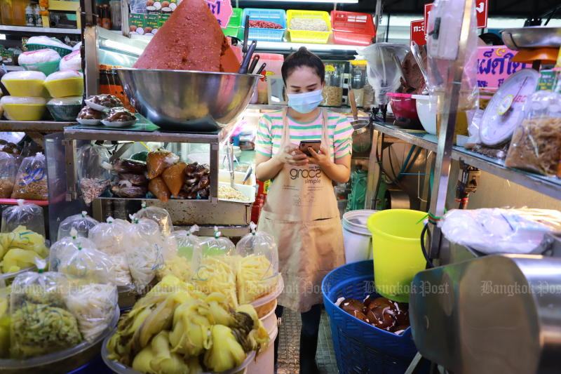 A food vendor uses her smartphone at Pak Nam market in Samut Prakan province on July 1, 2022. (Photo: Somchai Poomlard)