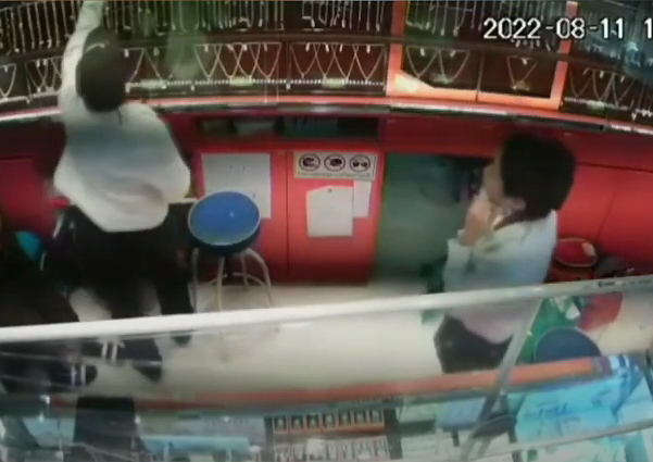 An armed man, left, reaches for a tray of gold necklaces at a gold shop in Ratchaburi province on Thursday. (Screenshot from security camera footage)