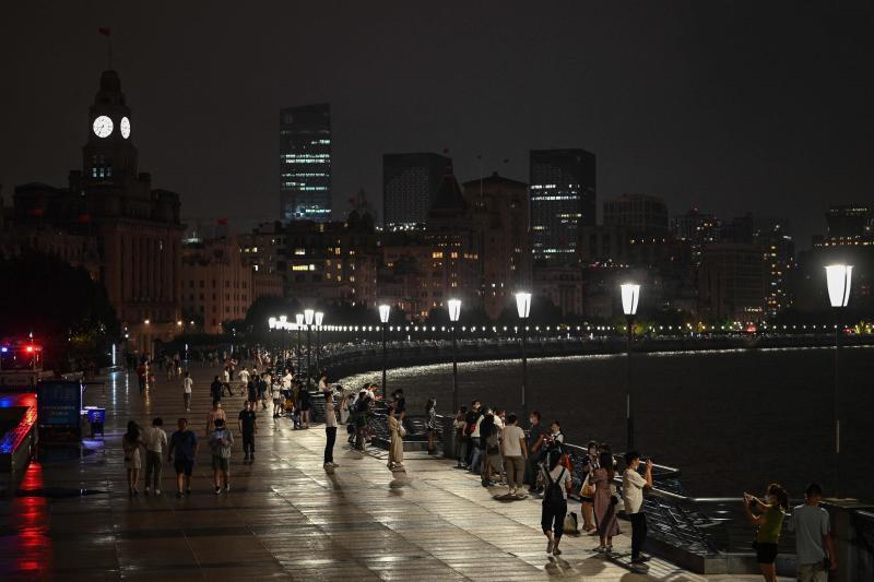 People walk along the Bund promenade along the Huangpu River as decorative lights are switch off as a measure to save energy in Shanghai on Aug 23, 2022. (Photo: AFP)