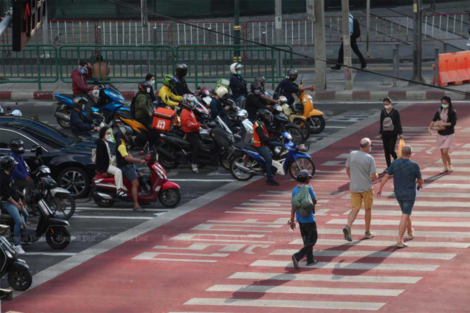 People cross a pedestrian crossing at the Asoke intersection in Bangkok while a motorcyclist encroaches on the space, which is a violation of traffic rules. (File Photo: Apichart Jinakul)