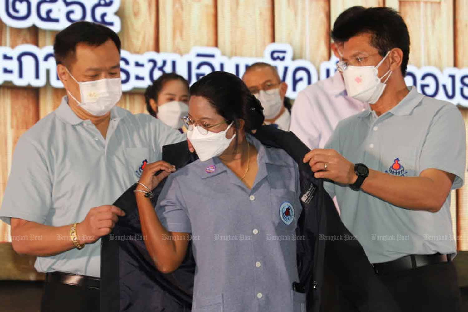 Public Health Minister Anutin Charnvirakul, left, and his deputy Sathit Pitutecha, right, present a jacket to an outstanding health volunteer, on a national day honouring health volunteers, in Nonthaburi province in March. (Photo: Apichit Jinakul)