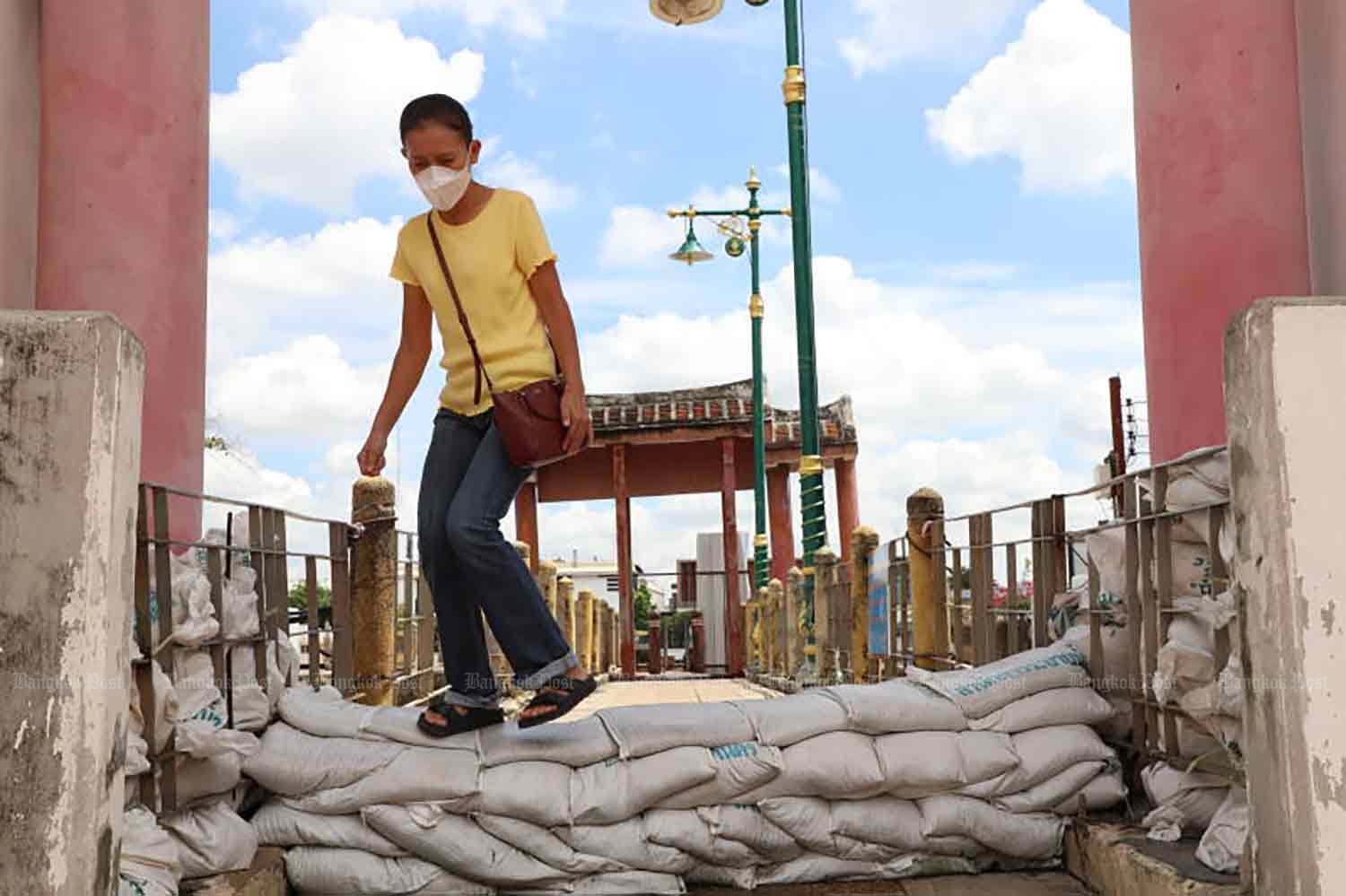 A woman crosses a sandbags barrier, built to keep out rising water from the Chao Phraya River, at the Kuan An Keng Shrine in the old Kudi Jin community in Thon Buri district. (Photo: Apichart Jinakul)