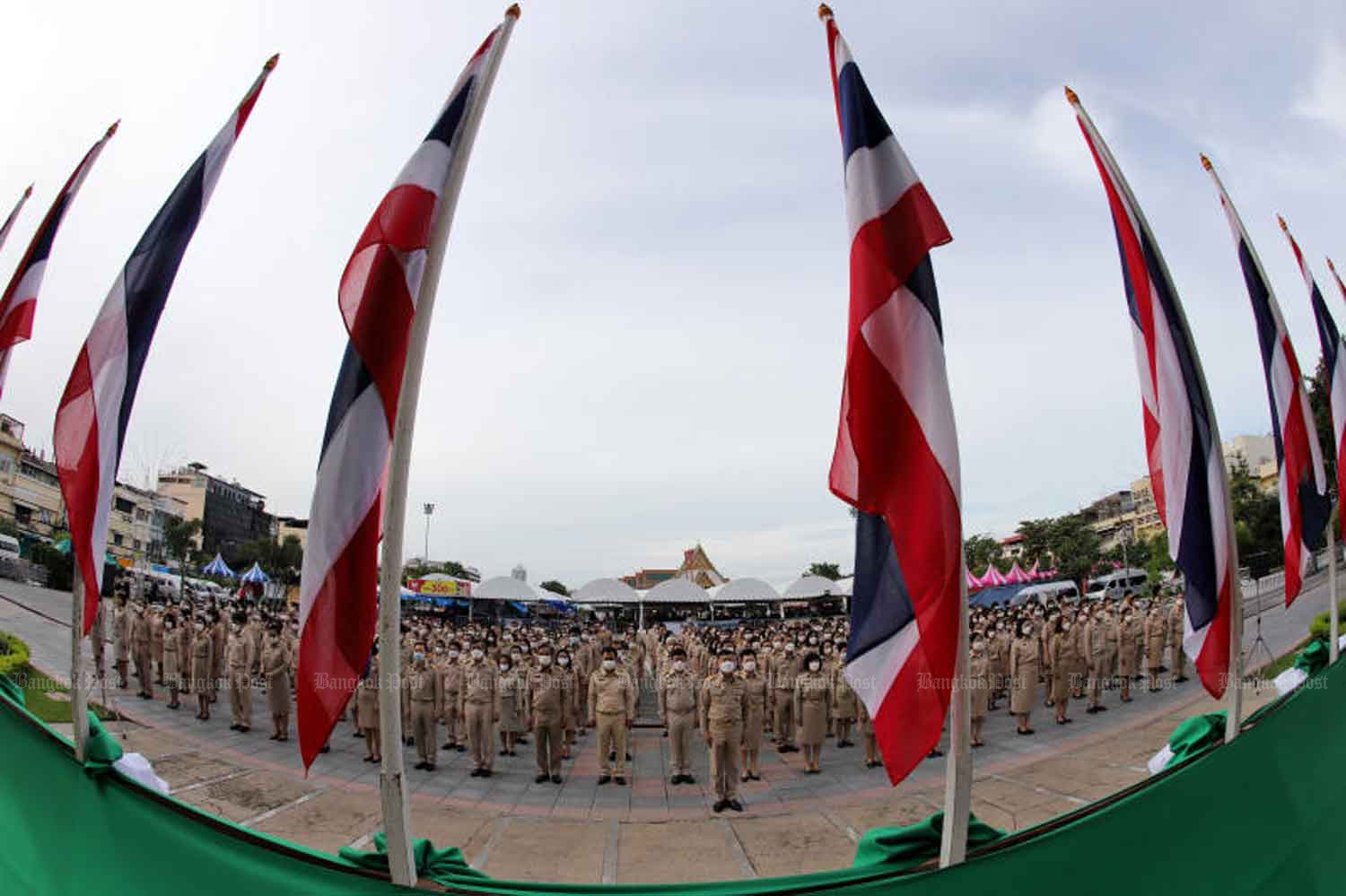 Officials led by City Clerk Khachit Chatchawanit attend a ceremony to mark National Flag Day in the plaza outside the Bangkok Metropolitan Administration headquarters on Wednesday when the country logged 637 new Covid-19 inpatients and 10 more fatalities related to the disease. (Photo: Chanat Katanyu)