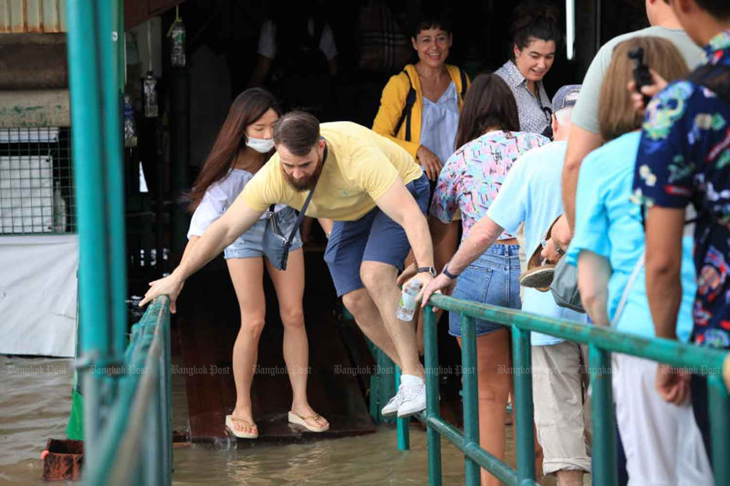 A tourist tries to keep his shoes dry while using the flooded pier at the Temple of Dawn beside the Chao Phraya River in Bangkok on Monday. (Photo: Apichart Jinakul)