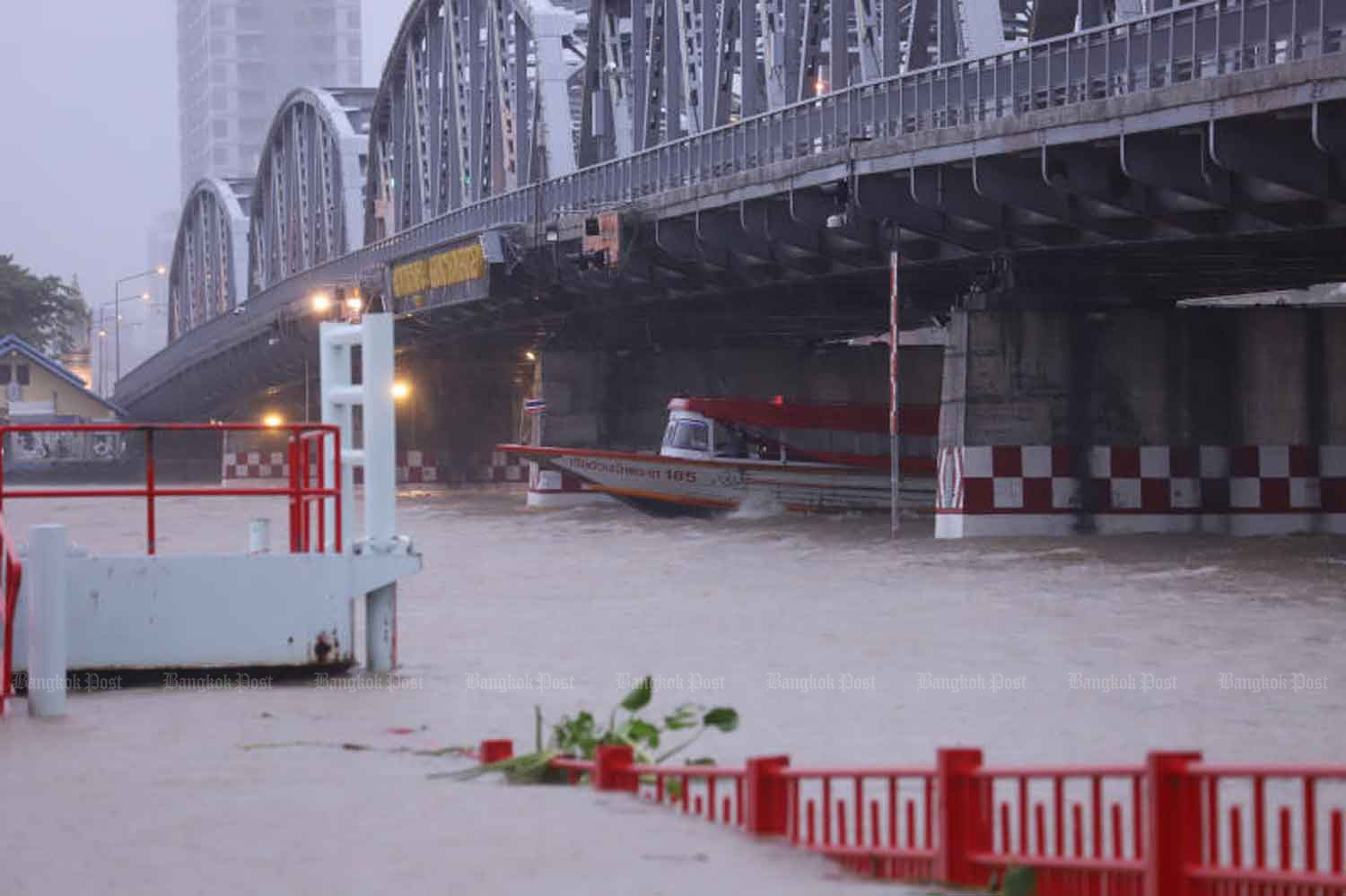 A commuter boat emerges from underneath the Krung Thon Bridge in Bangkok during a downpour on Thursday. The Chao Phraya has risen markedly in recent weeks as water from upstream provinces, compounded by high tides, has raised the river’s level. (Photo: Pornprom Satrabhaya)