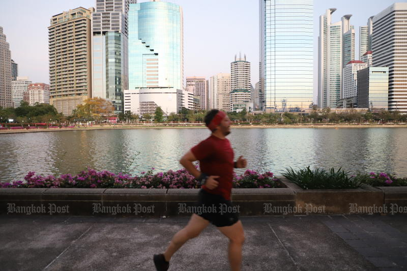 A man jogs in Benjakiti Park in Bangkok, with modern skyscrapers in the background. (Photo: Wichan Charoenkiatpakul)