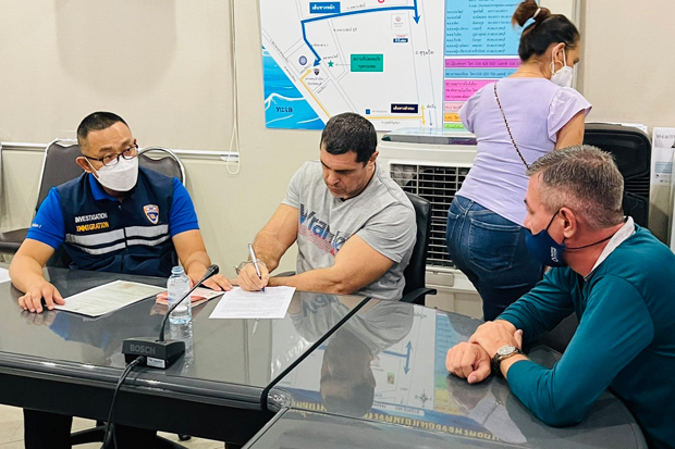 Igor Guzhin signs documents before immigration police after the Russian was arrested at Jomtien beach in Pattaya on Sunday. (Photo: Immigration Police Bureau)