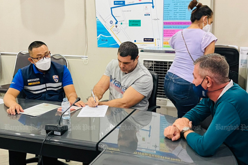 Igor Guzhin signs documents before immigration police after the Russian was arrested at Jomtien beach in Pattaya on Sunday. (Photo: Immigration Police Bureau)