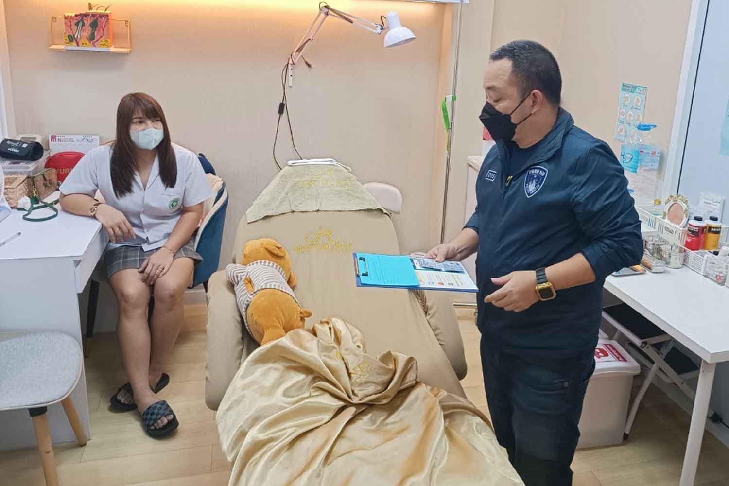 A police officer questions 36-year-old Srisunee Panyawat, left, who allegedly ran an illegal beauty clinic in Bang Khen district, Bangkok. (Photo: Royal Thai Police)