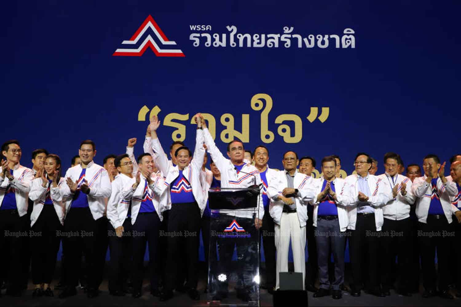 Gen Prayut Chan-o-cha, centre, is seen on stage raising the hand of United Thailand Nation party leader Pirapan Salirathavibhaga, and other key party members after the prime minister joined the party at its general assembly at the Queen Sirikit National Convention Centre on Monday. (Photo: Wichan Charoenkiatpakul)