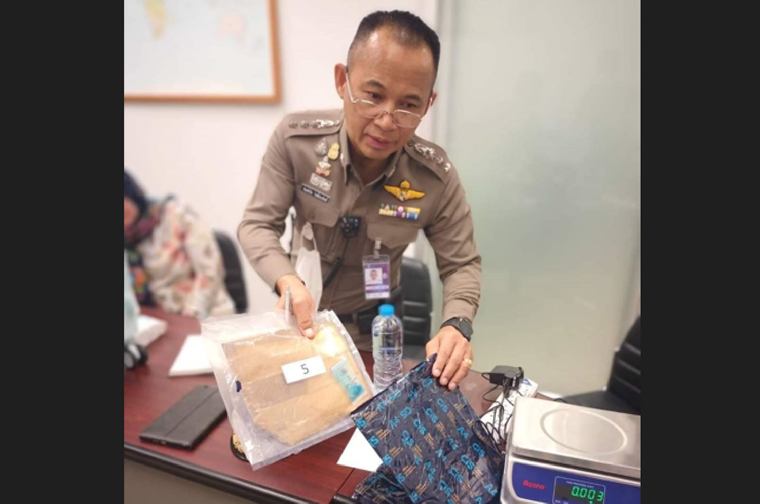 A police officer examines cocaine seized from a notebook computer's bag of a 41-year-old Uzbek woman, left, at Phuket airport on Friday. (Photo: Achadthaya Chuenniran)