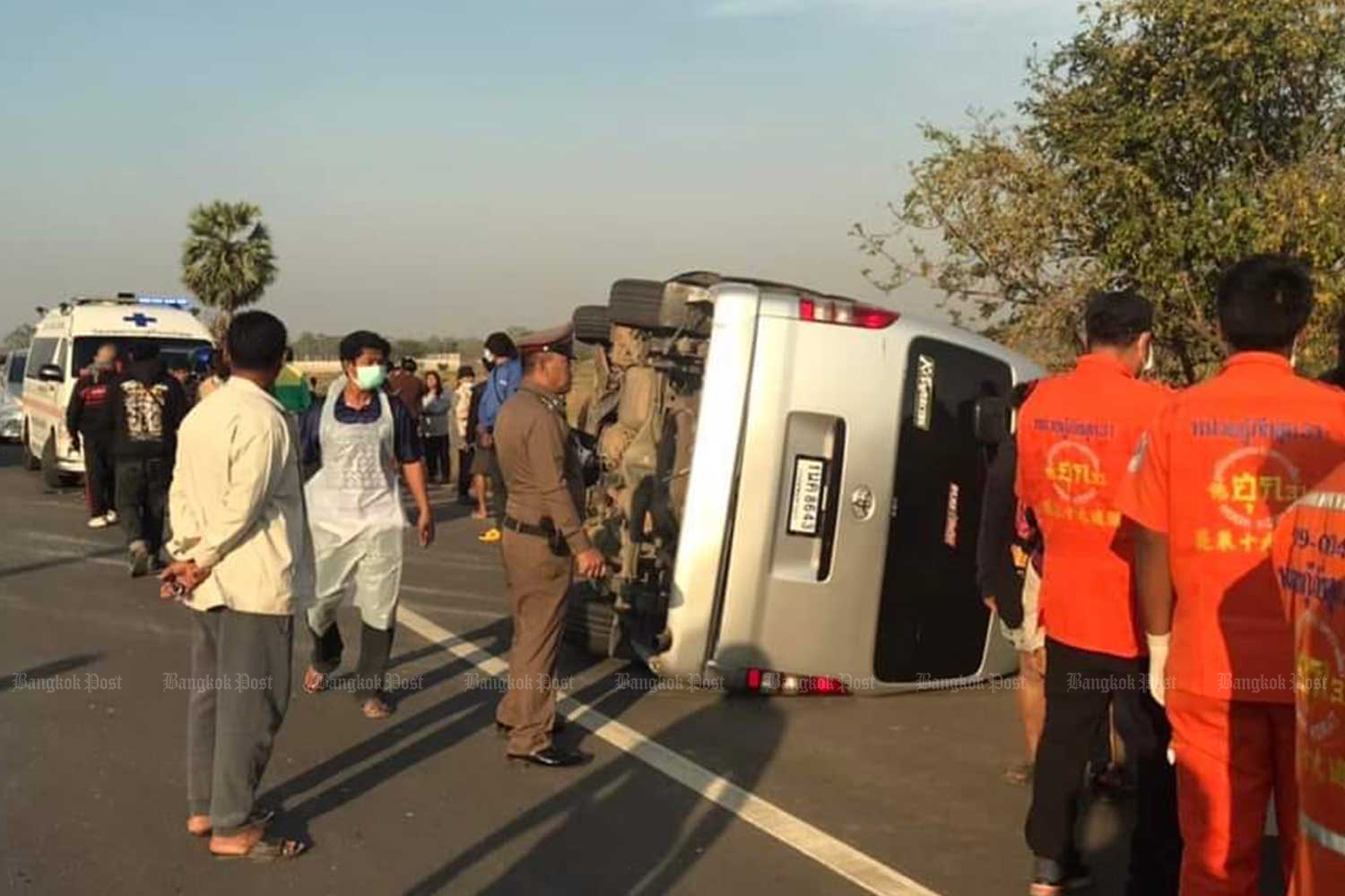 A police officer inspects an overturned school van in Non Thai district of Nakhon Ratchasima as rescue workers prepare to take injured students to a nearby hospital on Thursday morning. (Photo: Hook31 rescue team Facebook page)