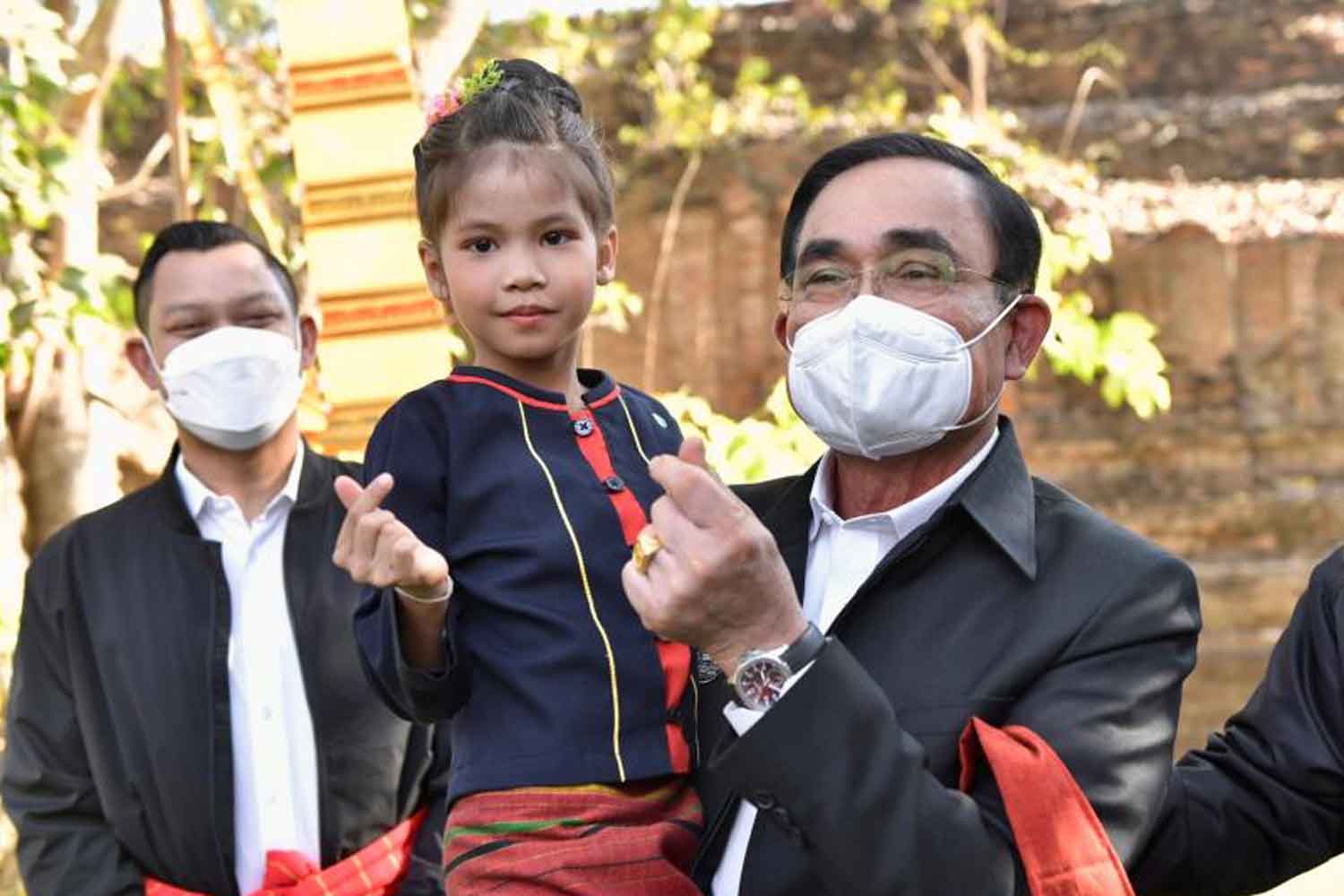 Prime Minister Prayut Chan-o-cha lifts a girl up in his arm as they make a ‘mini-heart’ gesture during his visit to follow up on the progress of community-based and cultural tourism projects in Muang district of Ratchaburi on Jan 19. (Government's photo)