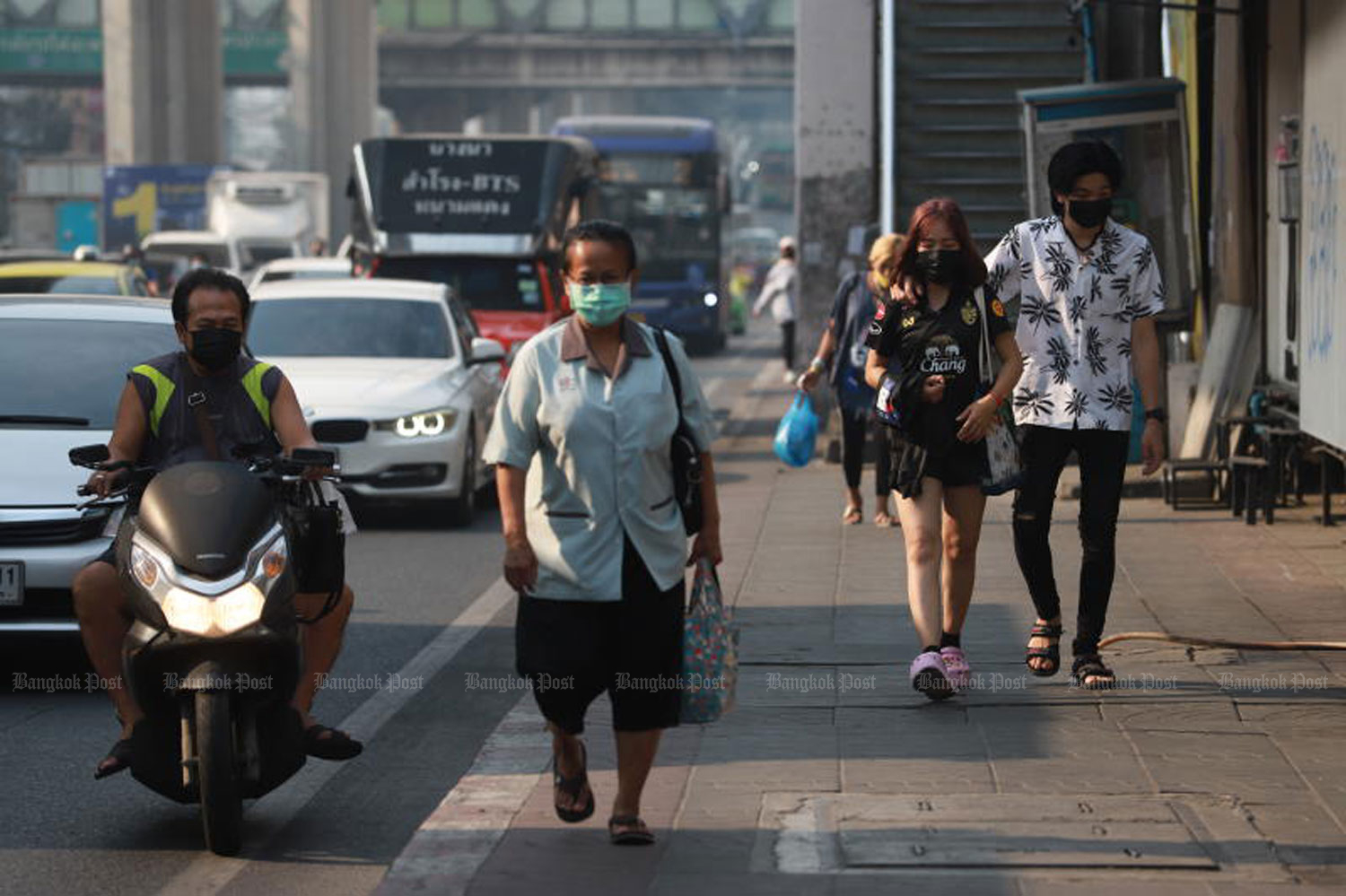 People, wearing face masks, walk along a road in Bang Na district of Bangkok around noon on Thursday as many areas are blanketed with smog. (Photo: Somchai Poomlard)