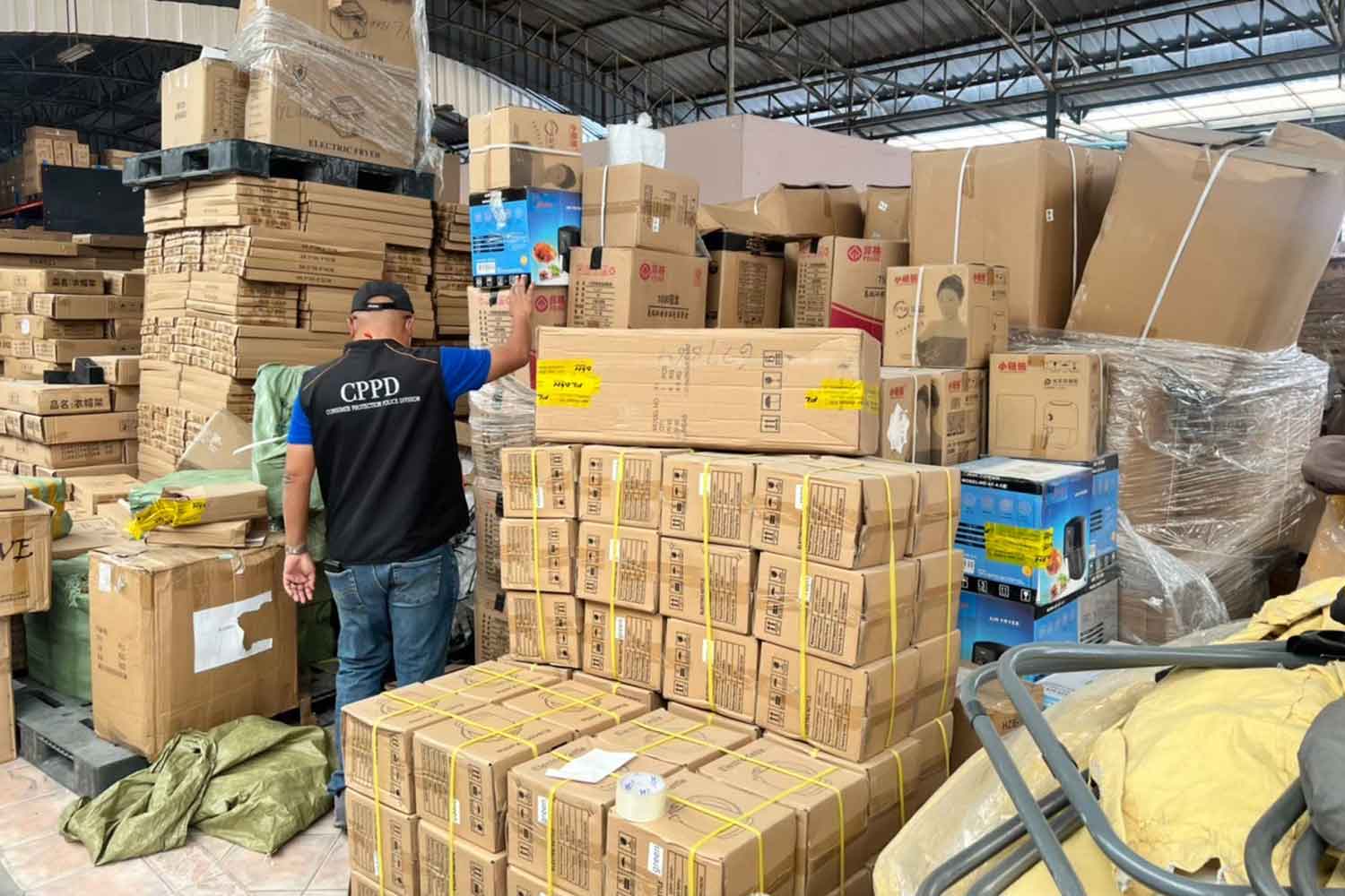 A consumer protection police officer examines boxes of fake products found in a warehouse in Samut Prakan's Bang Phli district on Feb 7. (Photo supplied)