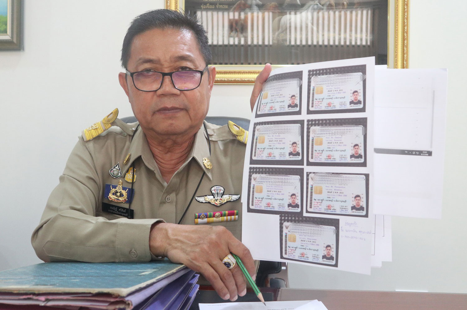 Thananat Srisat, chief of Kanchanaburi's Muang district, shows seven ID cards using the details and a picture of Phakin Sutpraphan, a 33-year-old owner of a coffee shop in tambon Lat Ya of the province. (Photo: Piyarat Chongcharoen)