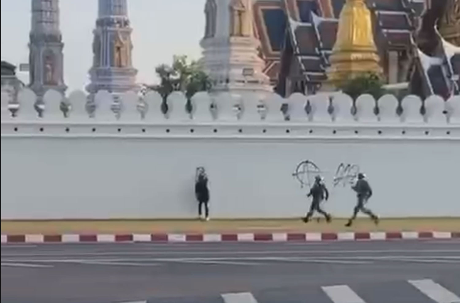 Two police officers rush to arrest a man using black spray paint to write and then cross out the number 112 on the wall of the Temple of the Emerald Buddha in Bangkok on Tuesday evening. (Capture from video)