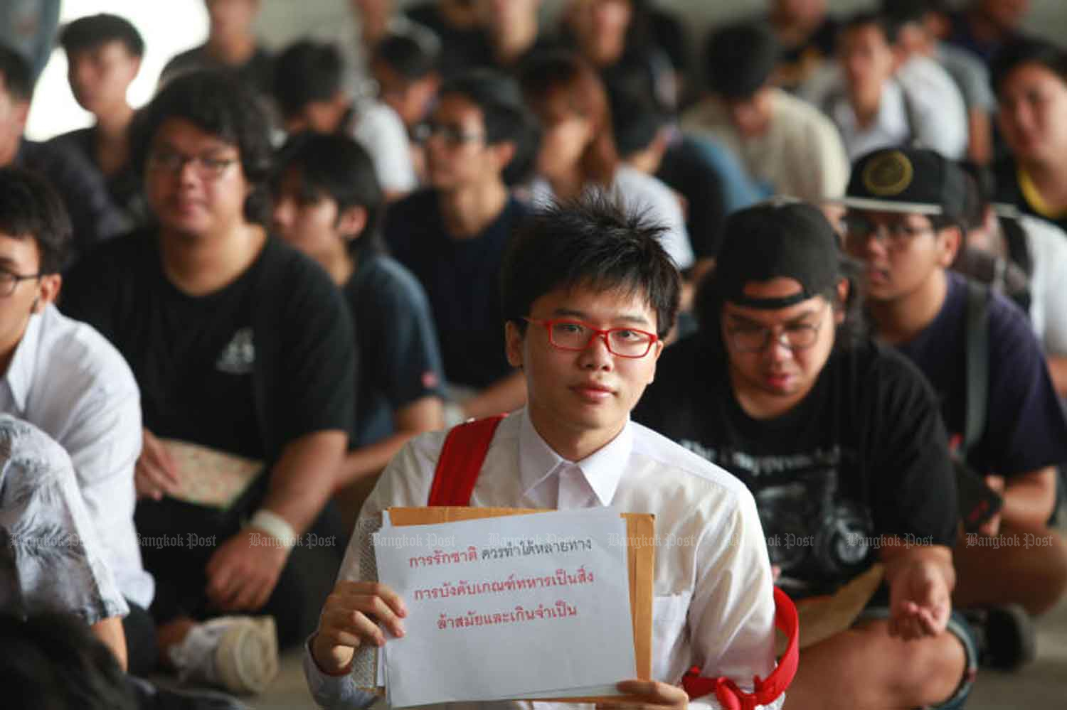 Student activist Netiwit Chotiphatphaisal holds a sign denouncing the compulsory military draft as ‘obsolete and unnecessary’ at a conscription unit at Wat Rat Phothong in Samut Prakan, where he went to seek student deferment of his military service, in 2017. (Photo: Somchai Poomlard)