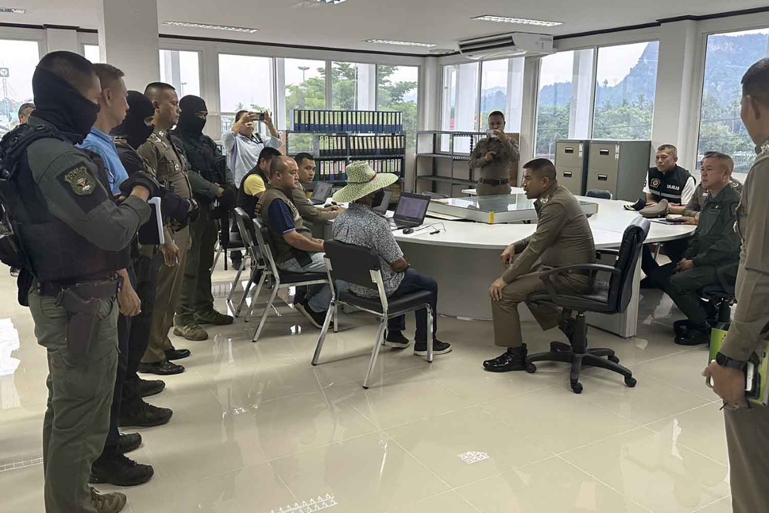 Deputy police chief Pol Gen Surachate Hakpak, seated right, interrogates Manop Wang-ngan, seated and wearing a wide-brim hat, at Khirira Nikhom police station in Surat Thani after his arrest on Monday afternoon. (Photo: Supapong Chaolan)