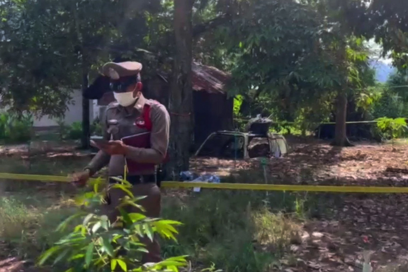 A policeman stands near a discarded pickup truck cap, where the body of a 47-year-old man was discovered, in Wiang Sa district of Surat Thani. (Screen capture)