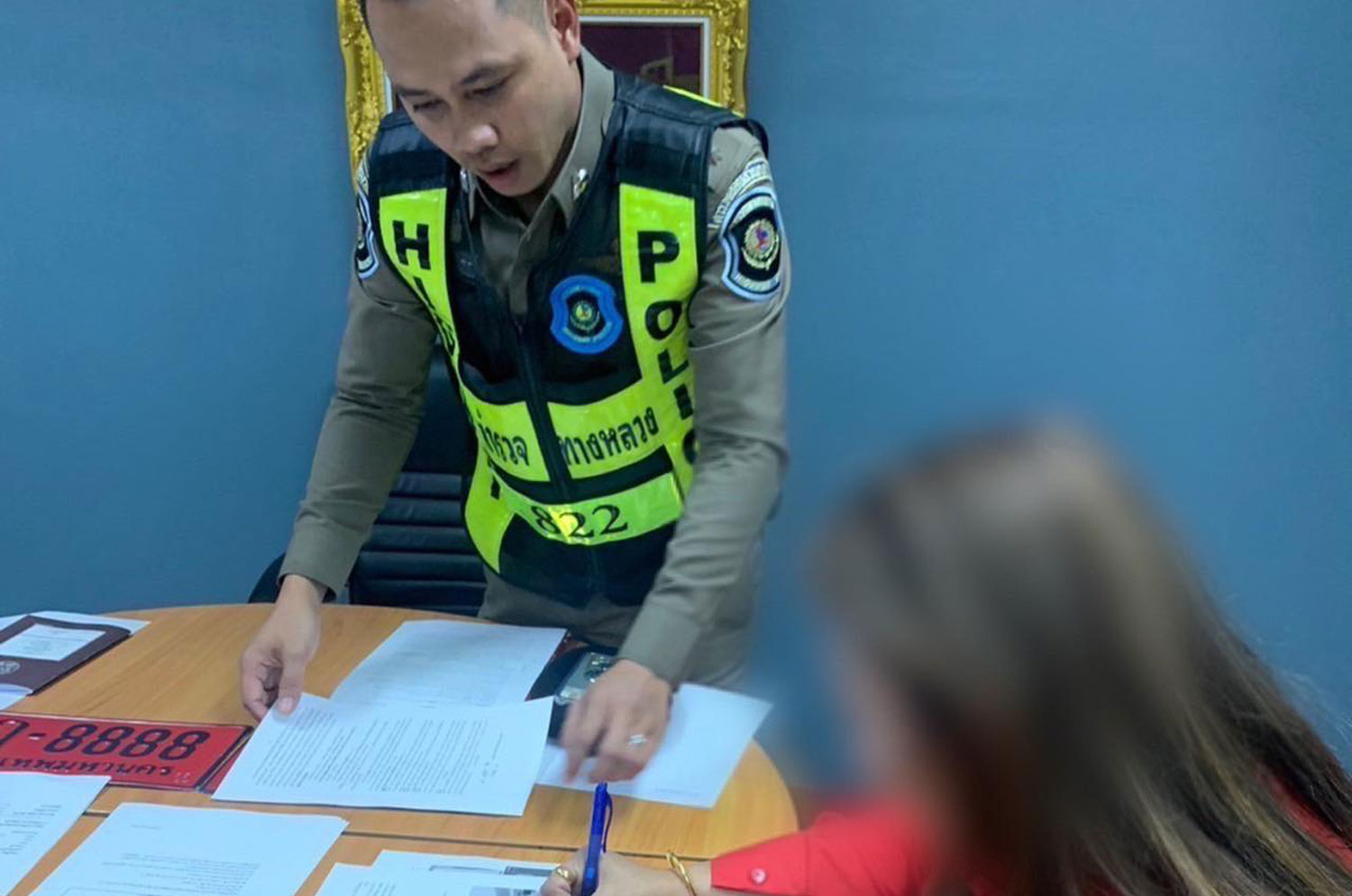 The 35-year-old woman signs a document acknowledging police charges after she was arrested in Pathum Thani province with fake licence plates on her BMW car and hundreds of unpaid toll fees. (Photo: Central Investigation Bureau)