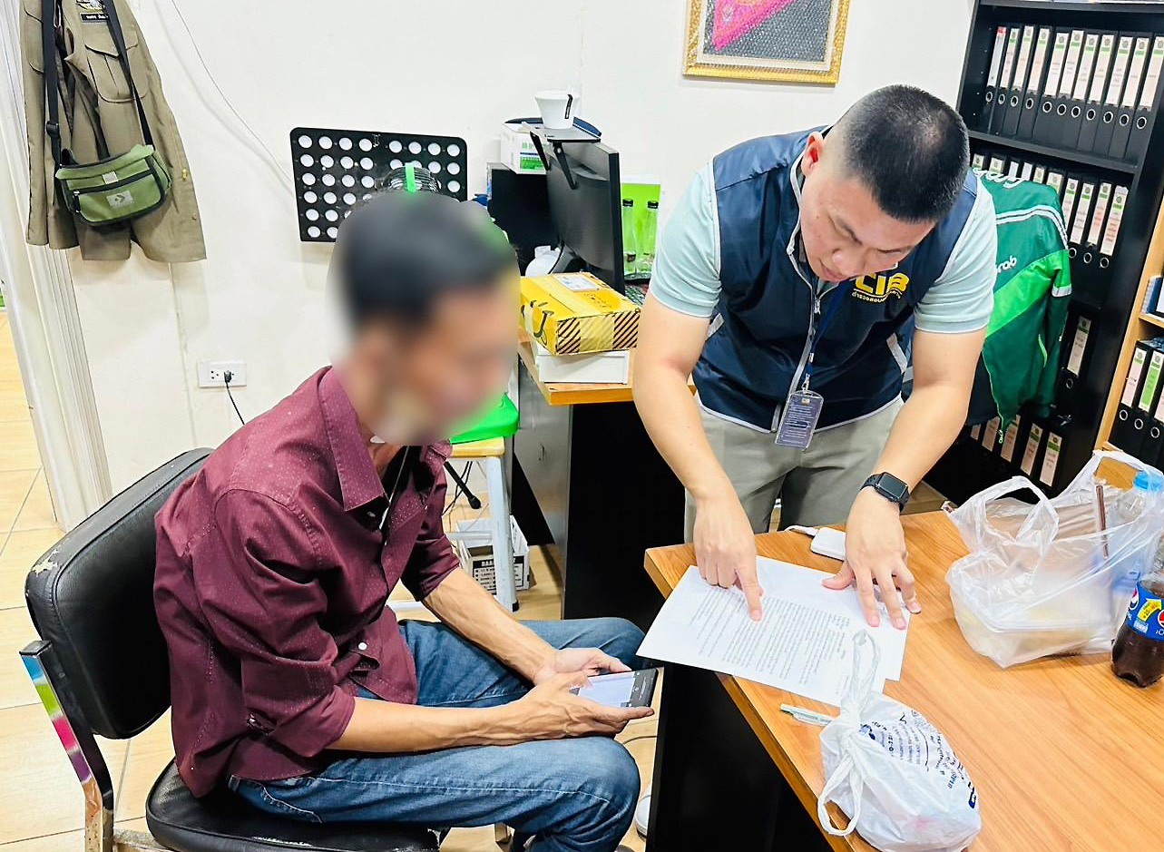 An officer questions a former insurance salesman about creating fake policies and duping victims following his arrest in Chon Buri on Saturday. (Photo: Central Investigation Bureau)