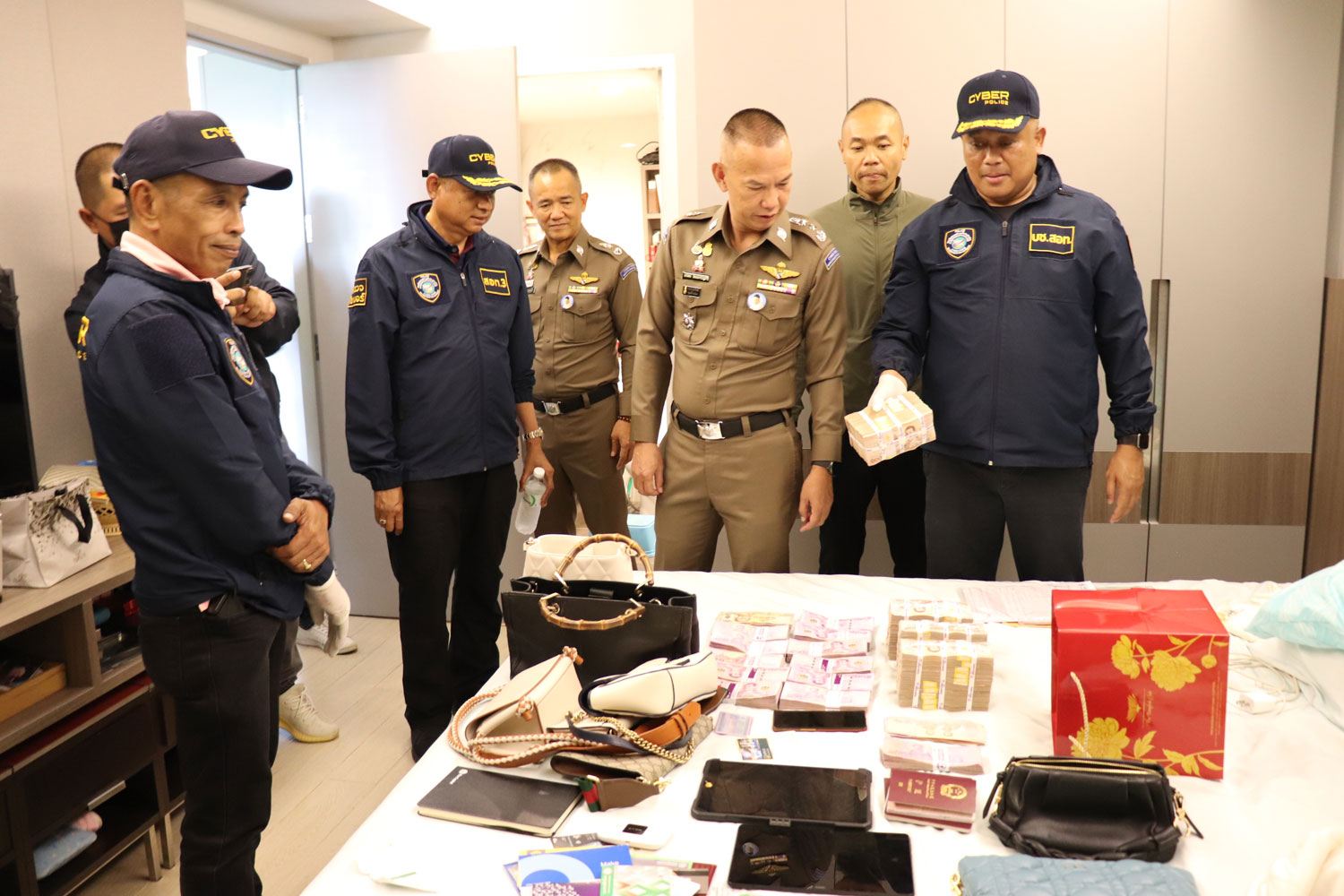 Pol Lt Gen Worawat Watnakhonbancha, chief of the Cyber Crime Investigation Bureau, and his team inspect cash, passports and valuables seized from a Chinese couple during a raid to crack down on a cryptocurrency scam network. (Photo supplied/Wassayos Ngamkham)