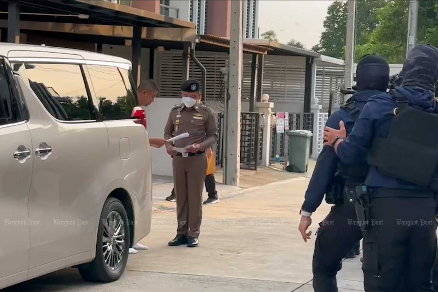 Deputy national police chief Pol Gen Surachate Hakparn (left, partly concealed) reads the court search warrant, near his house in Bangkok on Monday morning. (Photo supplied)