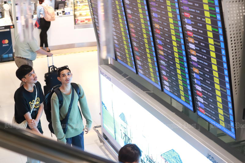 Passengers check the flight status board at Suvarnabhumi airport in Samut Prakan on Saturday. (Photo: Somchai Poomlard)