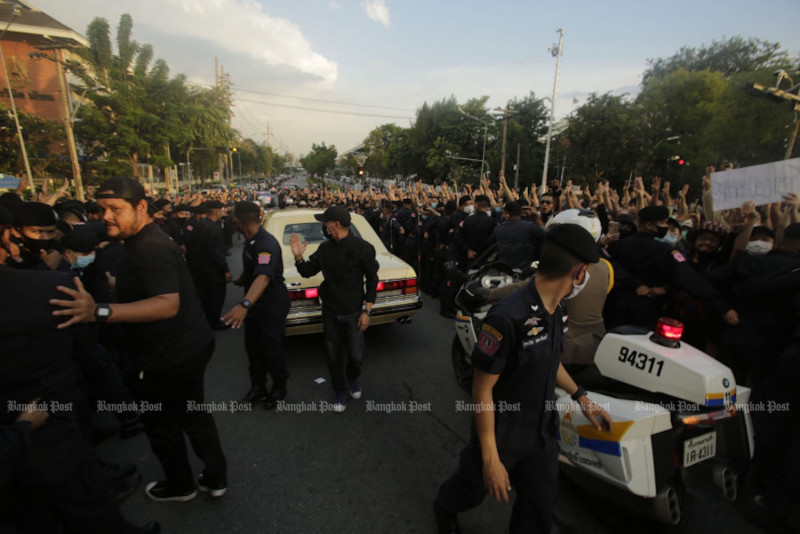 The royal motorcade of Her Majesty the Queen drives down Phitsanulok Road as security officers try to stop protesters flashing three-finger salutes on Oct 14, 2020. (Bangkok Post File Photo)