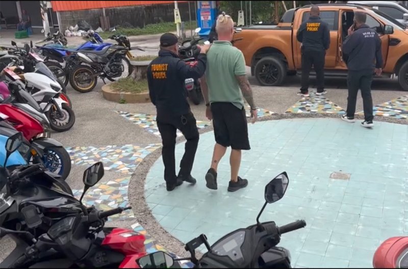 Ein Beamter der Touristenpolizei begleitete am Dienstagabend den festgenommenen russischen Staatsbürger Valerii Belomyttcev aus der durchsuchten Autovermietung auf Koh Phangan in der Provinz Surat Thani. (Foto: Touristenpolizei)