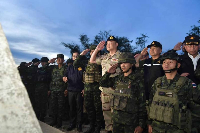 Prime Minister Anutin Charnvirakul, wearing a territorial defence volunteer uniform, salutes the Thai national flag and then joins in singing the national anthem, at Phu Makua military base on the border in Si Sa Ket province on Tuesday evening. (Photo: Government House)